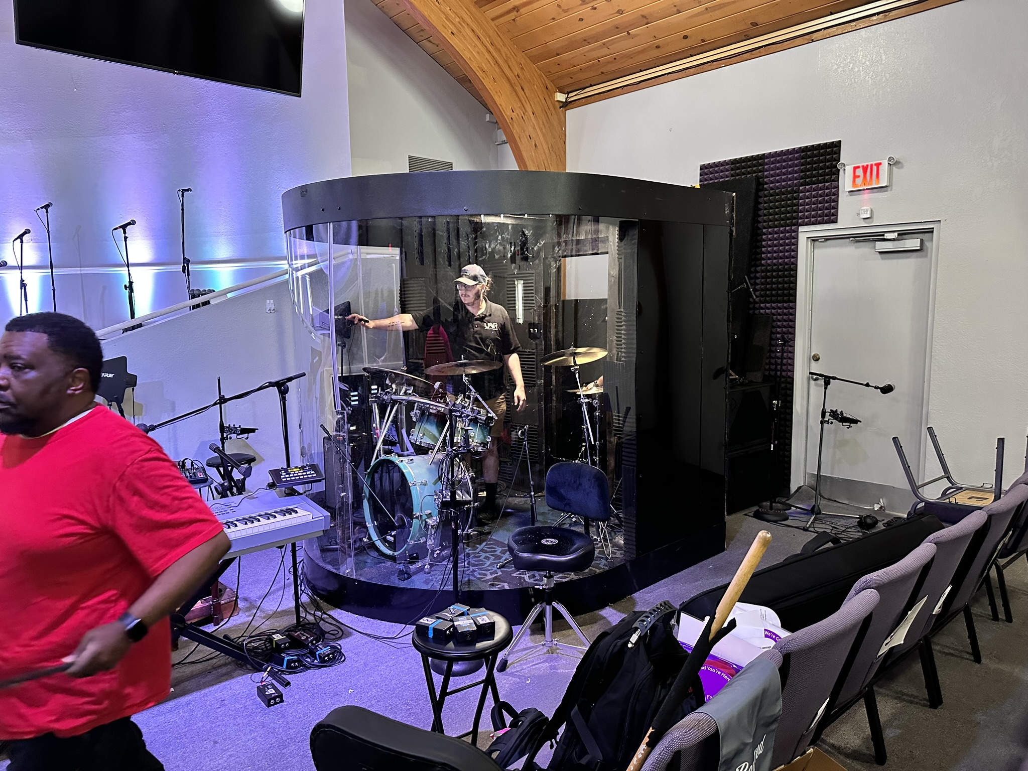 Custom curved acrylic drum shield enclosure installed in a church worship space with drummer performing