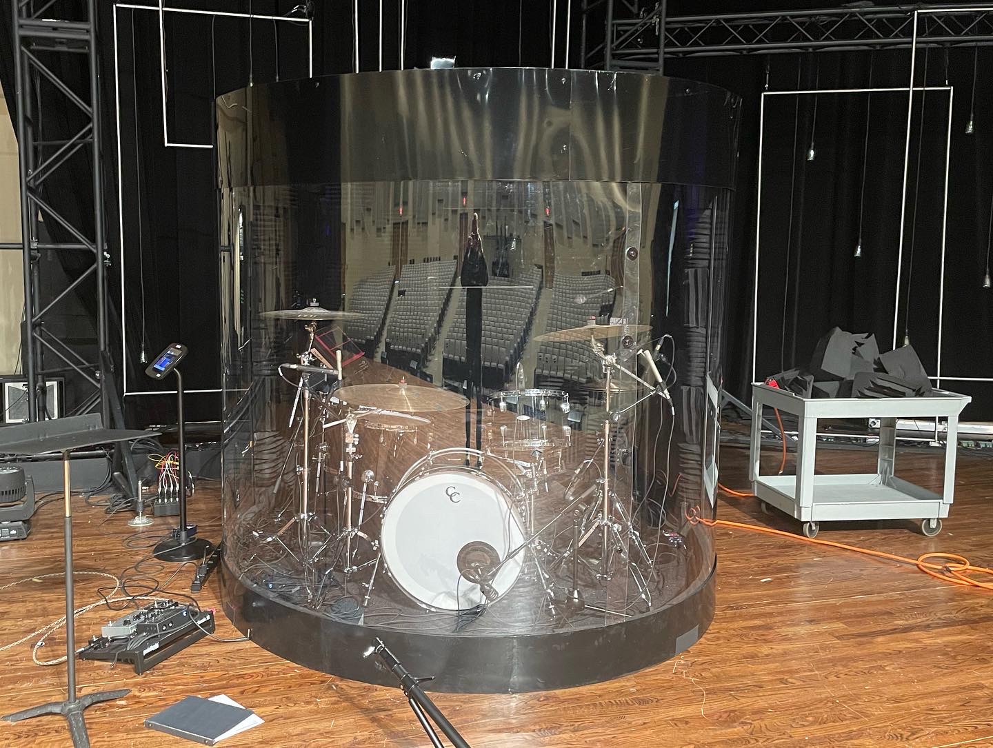 Custom curved acrylic drum shield enclosure surrounding a full drum kit on a large auditorium stage