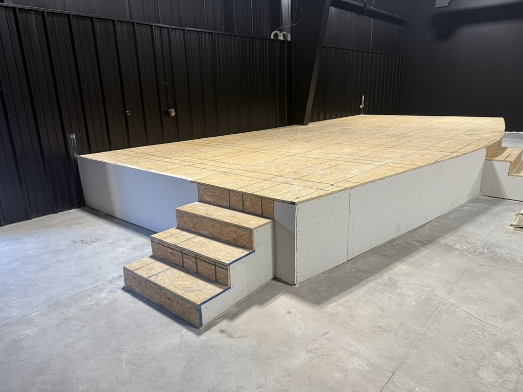 Steel-framed stage platform under construction with built-in steps inside a commercial metal building