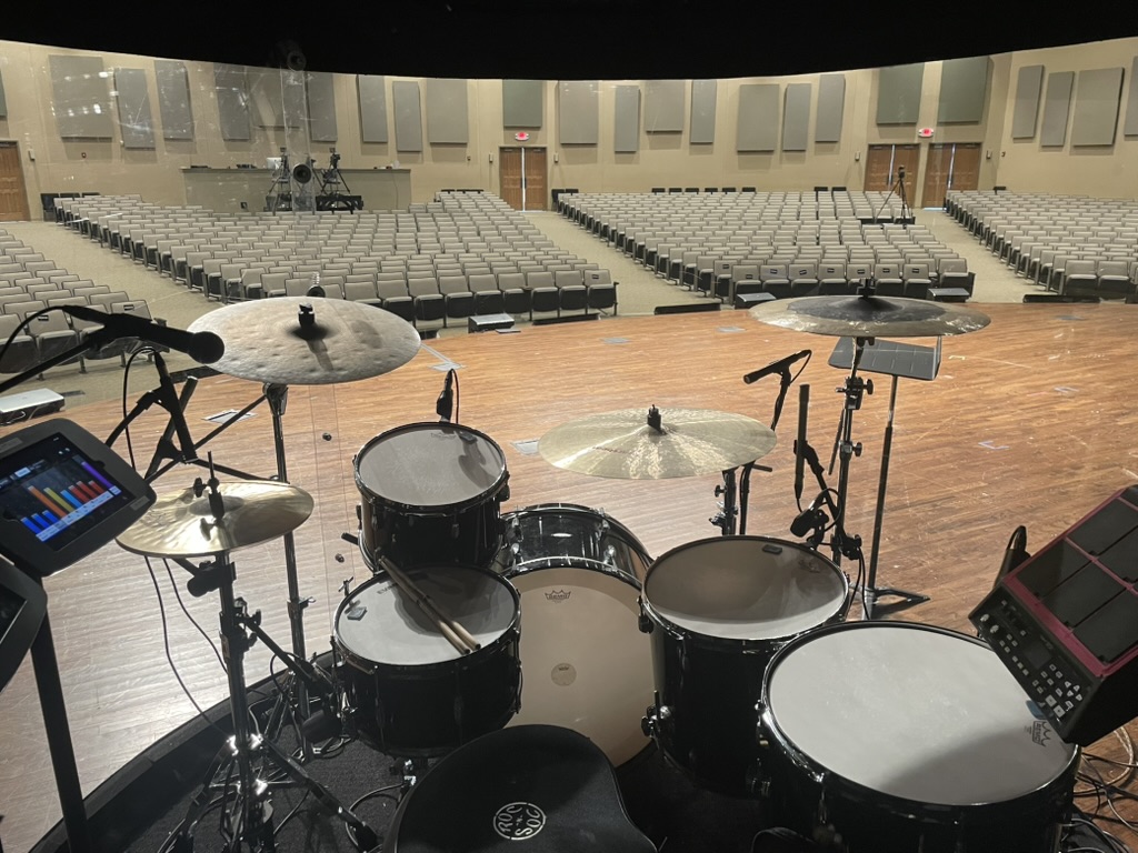 View from inside a custom acrylic drum shield looking out at a large church auditorium with full drum kit visible