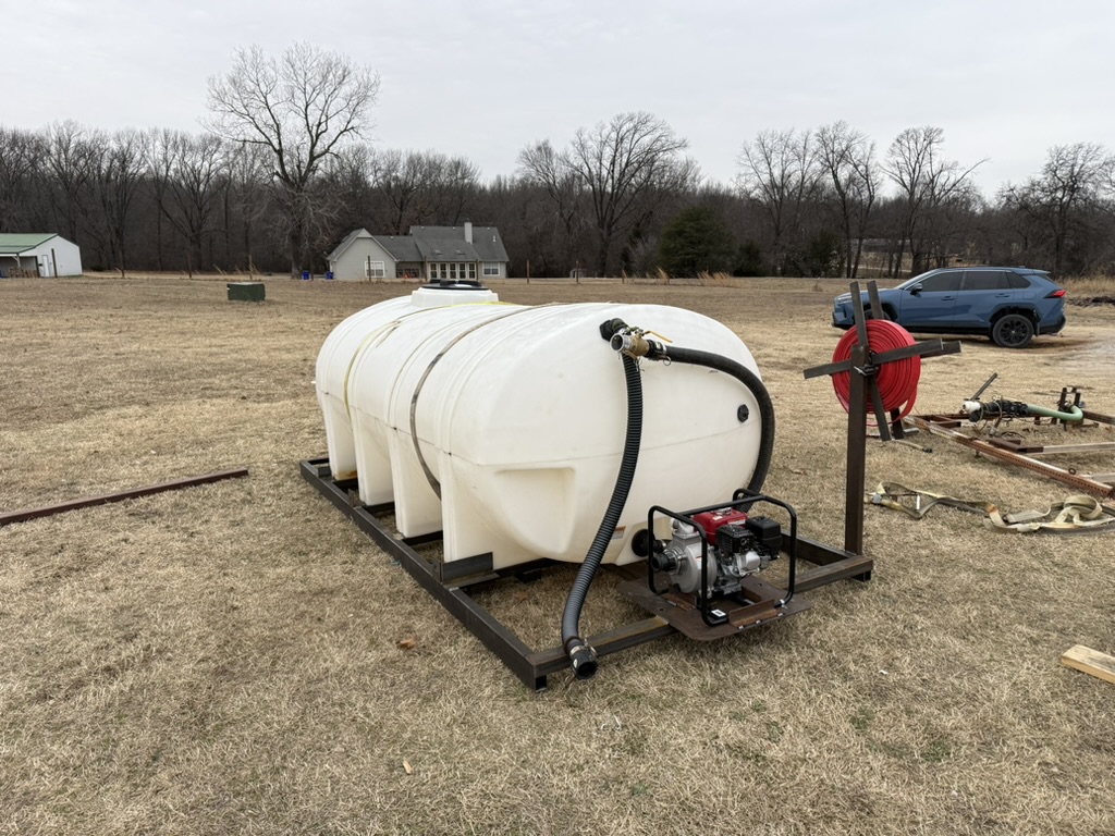 Large water tank mounted on a custom welded steel skid with gas-powered pump and hose reel